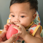 A baby drinking from a Tiny Cup held by a parent